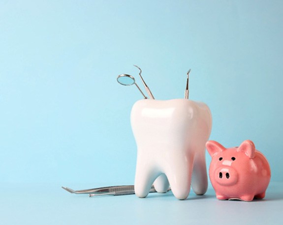 Pink piggy bank and tooth model with medical instruments on blue background