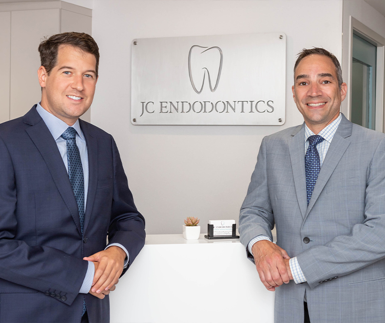 Two smiling endodontists at front desk of J C Endodontics Root Canal Specialists in New York City