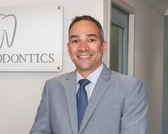 Doctor Jacobson smiling in front of sign on wall for J C Endodontics Root Canal Specialists