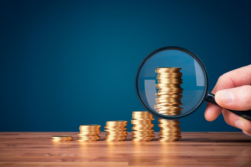 Stacks of coins compared with magnifying glass